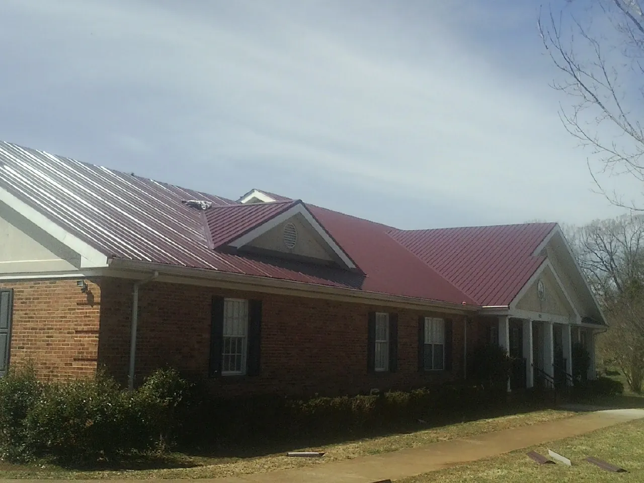 Red metal roof with gabled entries on a long brick building, from a Hail Damage Roof Repair job in Arena