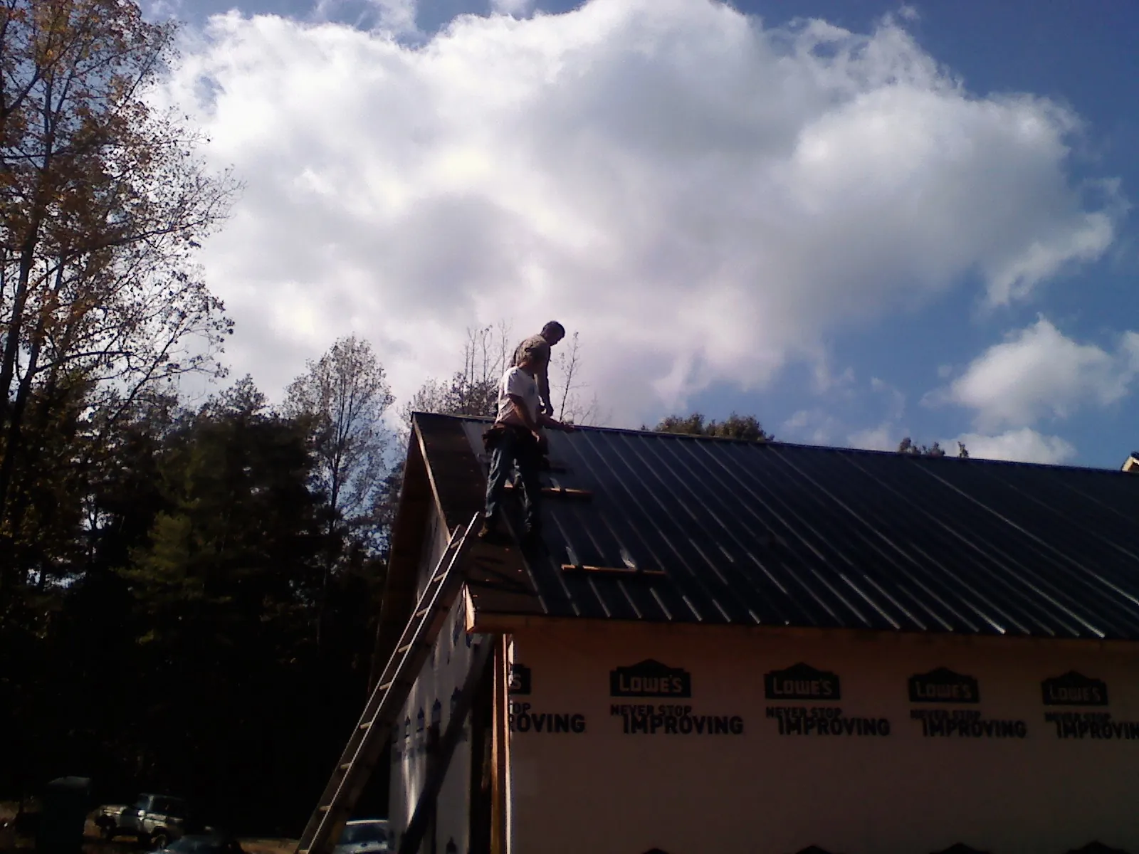 Roofer fastening dark metal panels high against a cloudy sky, from a Roof Inspection job in Arena