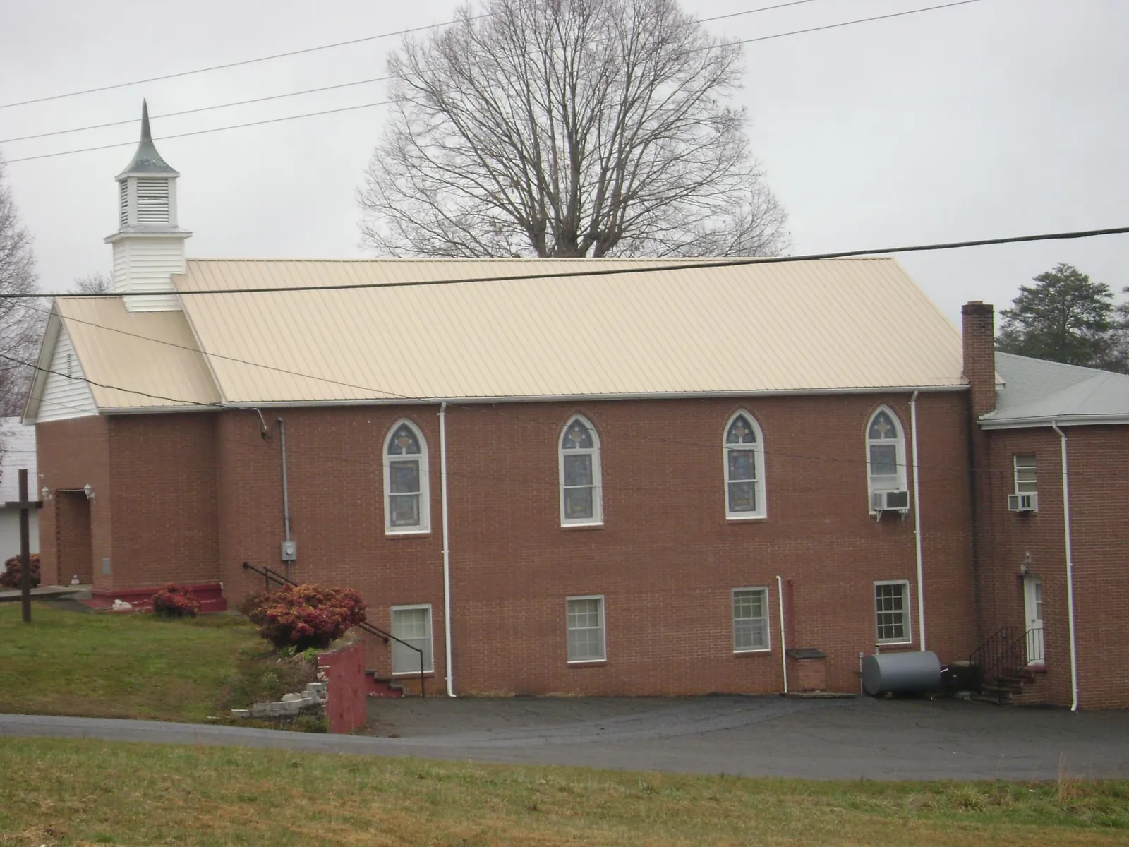 New tan metal roof on a brick church with a white steeple in Arena