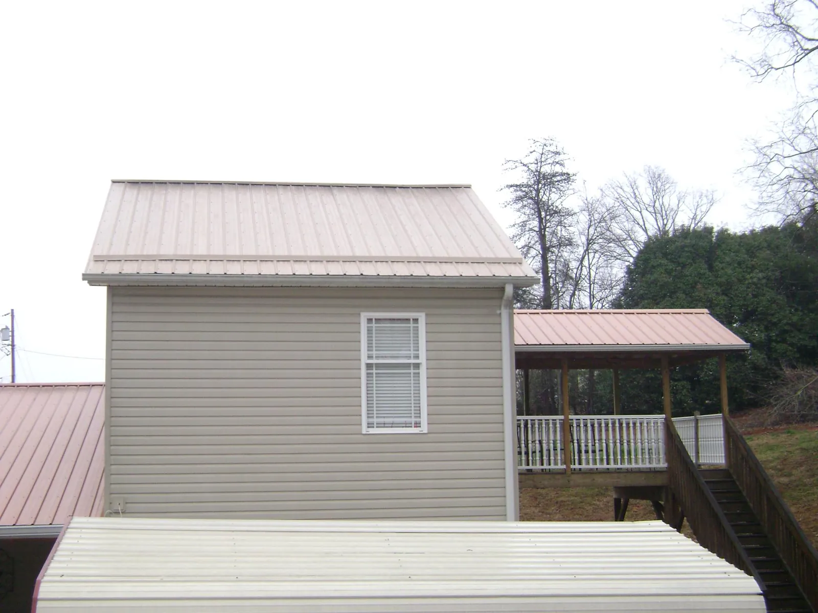 Tan metal roofs on a two story addition and attached porch, from a Roof Replacement job in Arena